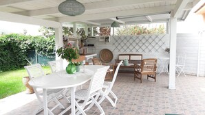 Ein überdachter Patio-Bereich mit rundem Tisch und Stühlen, einer hängenden Leuchte und einem an der Wand befestigten Radio.