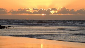 Een zonsondergang boven de oceaan, met golven die de kust naderen.