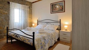 Ein Schlafzimmer mit einer Steinwand, einem Bett mit floralem Überwurf, zwei Nachttischen mit Lampen und einem gerahmten Bild an der Wand.
