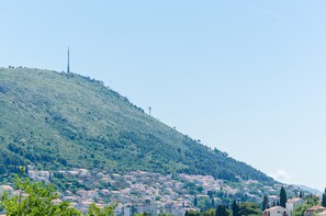 A hillside town with buildings spread across the slope, a prominent communication tower on the hilltop, and a clear sky. - Apartments Grga (Dubrovnik)