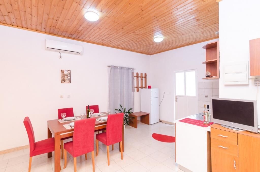 A dining area with a wooden table and red chairs, a small refrigerator, and a TV on a wooden cabinet.