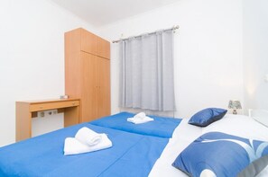 A hotel room with two beds, a wooden wardrobe, a desk, and a window with curtains. - Apartments Grga (Dubrovnik)