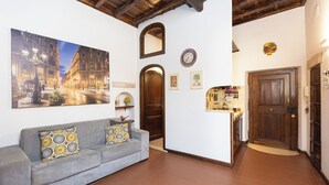 Un salon comprenant un canapé, un grand tableau, une porte en bois et un coin cuisine avec un réfrigérateur.