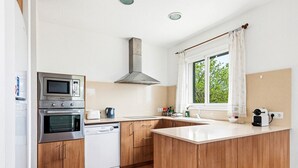 Une cuisine moderne dotée d’appareils électroménagers en acier inoxydable, de meubles en bois, d’une grande fenêtre avec des rideaux et d’un sol carrelé.