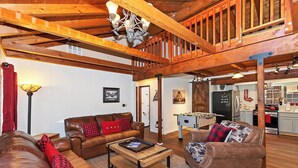 A spacious living room with leather sofas, a wooden coffee table, and a kitchen area visible through an open door.