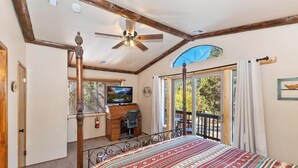A bedroom with a large bed, a ceiling fan, a TV, and a view of the outdoors through a window.