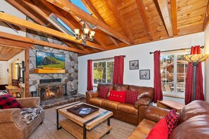 A cozy living room with a stone fireplace, leather sofa, and a television mounted on the wall. - Close to Bear Mountain & Golf Course! Hot Tub! Fenced Yard! Foosball! (Big Bear Lake)