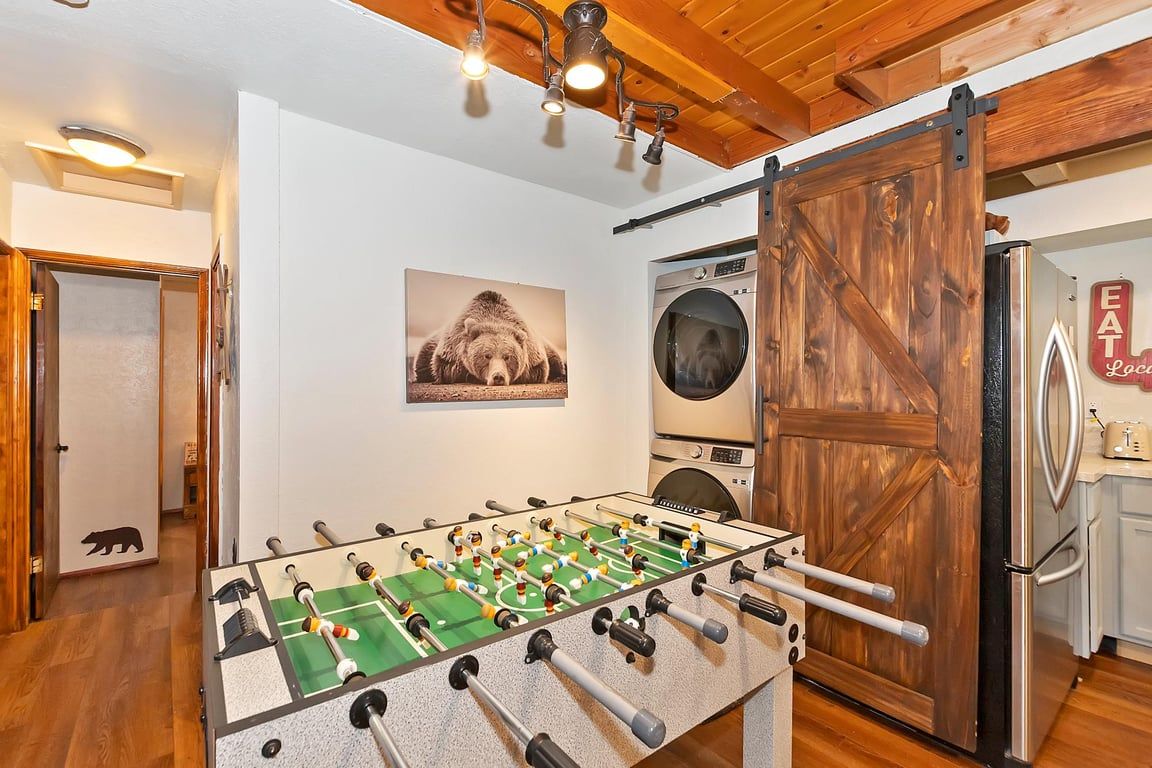 A room with a foosball table, a washing machine, and a refrigerator.
