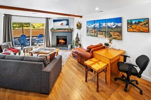 A modern living room with a fireplace, a sofa, a dining table, and a TV mounted on the wall.