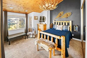A bedroom with a wooden bed, a bench, a dresser, and a window with a view of trees.