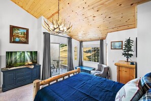 A bedroom with a bed, a dresser, a television, and a view of the outdoors.
