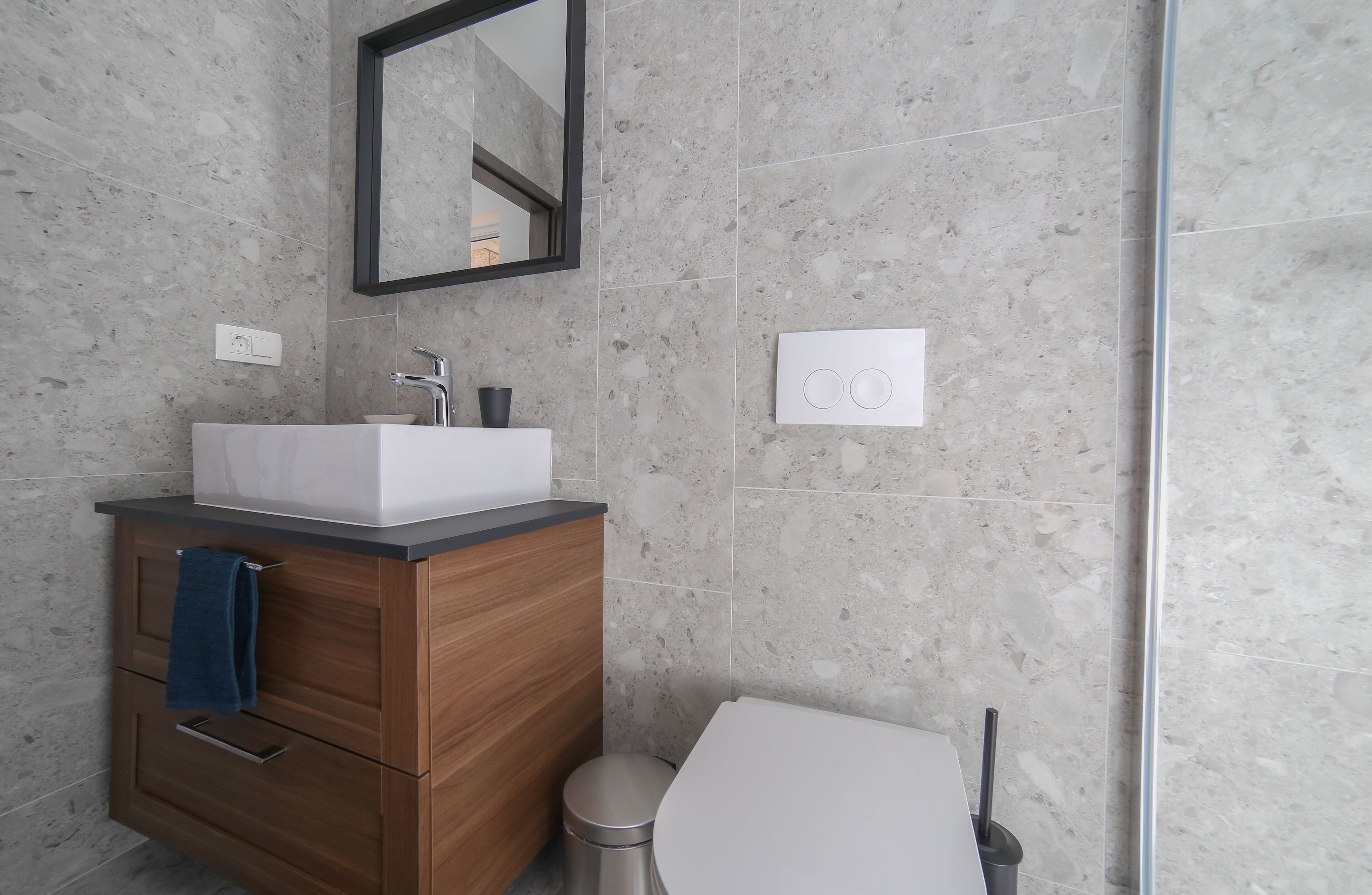 Ein modernes Badezimmer mit Marmorwand, Waschtisch aus Holz, weißem Waschbecken und Toilette.