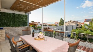 Un balcón con mesa dispuesta para comer, sillas alrededor, techo de madera y vista de la ciudad.