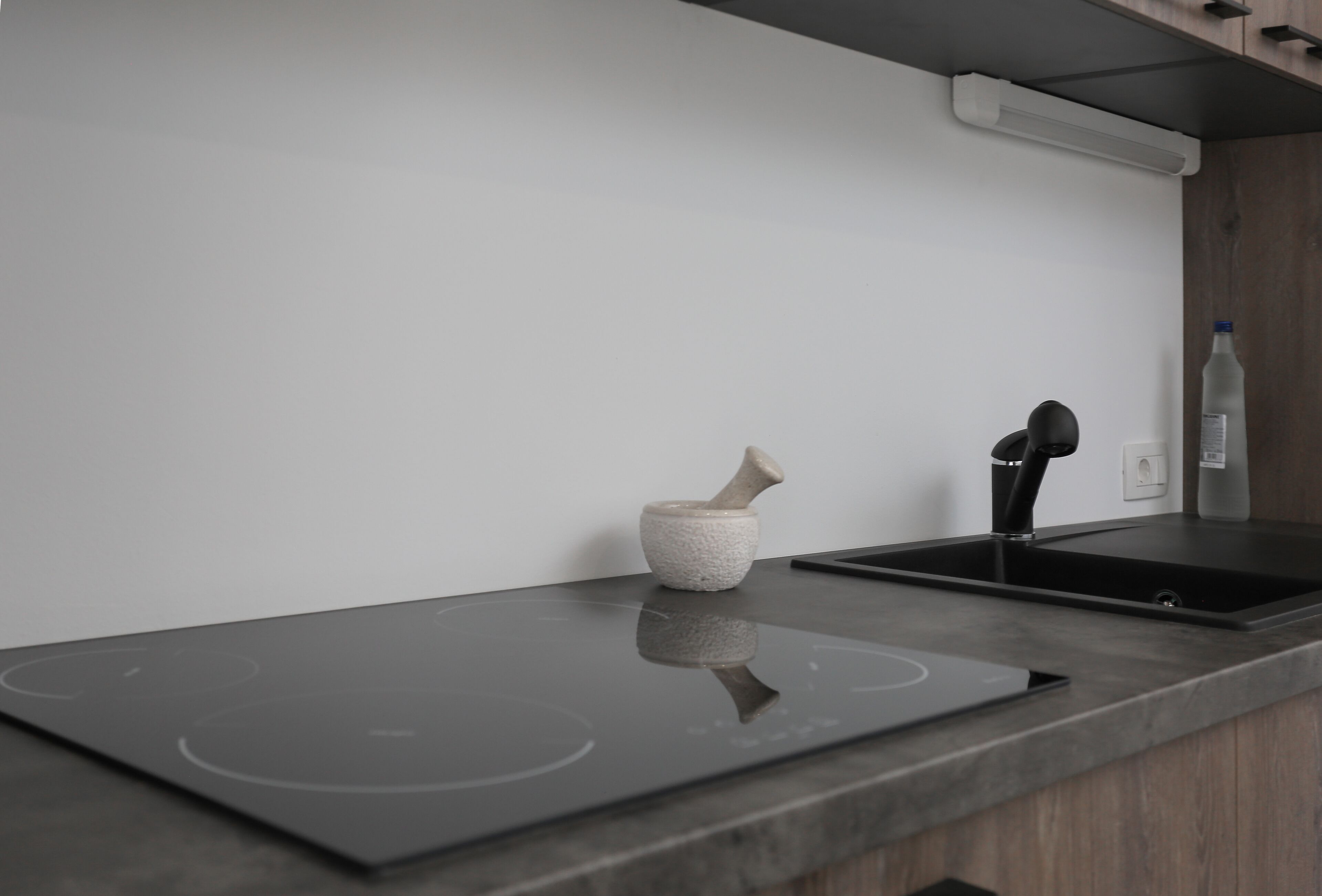A modern kitchen with a black induction cooktop, a stone mortar, and a black faucet.