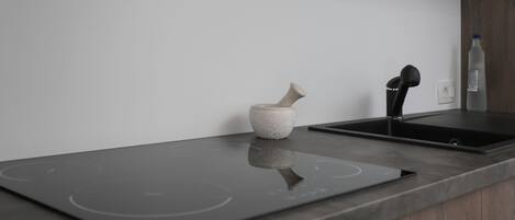 A modern kitchen with a black induction cooktop, a stone mortar, and a black faucet.