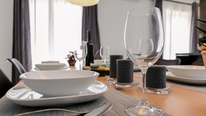Una mesa de comedor dispuesta con platos, tazones y cubiertos blancos, una copa de cristal transparente y velas sobre la mesa.