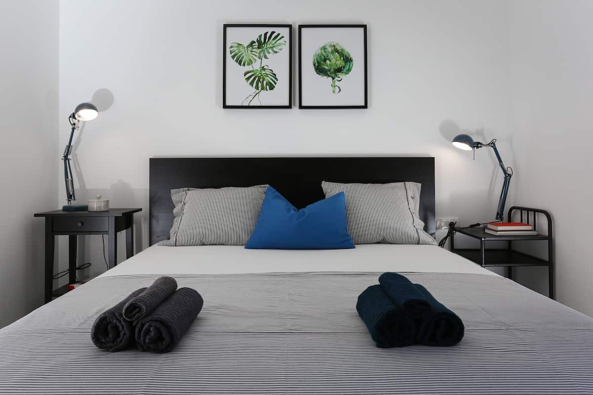A neatly made bed with striped bedding, two pillows, and rolled towels. There are two framed botanical prints on the wall above the bed.