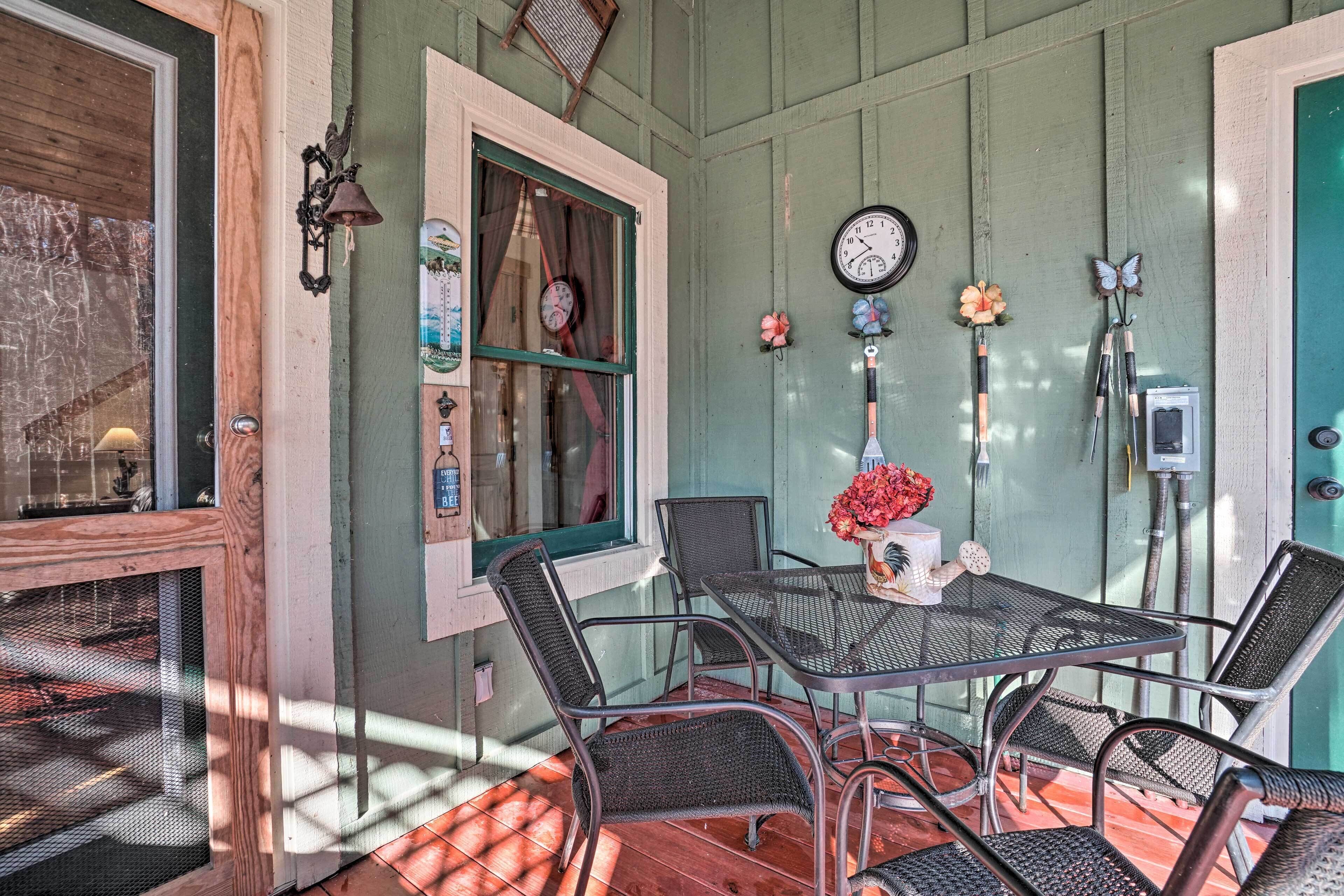 A cozy patio area with a metal table and chairs, a clock on the wall, and a window with curtains.