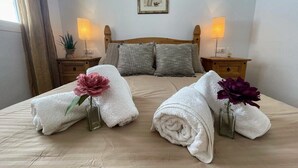 A neatly made bed with two towels and flowers, bedside tables with lamps, and a framed picture on the wall. - La Cinuelica 2 Bed, 1st Floor apt with comm pool R14.99 (Alicante)