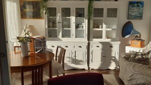 A dining area with a wooden table and chairs, a cabinet with glass doors, and a sofa with patterned cushions.