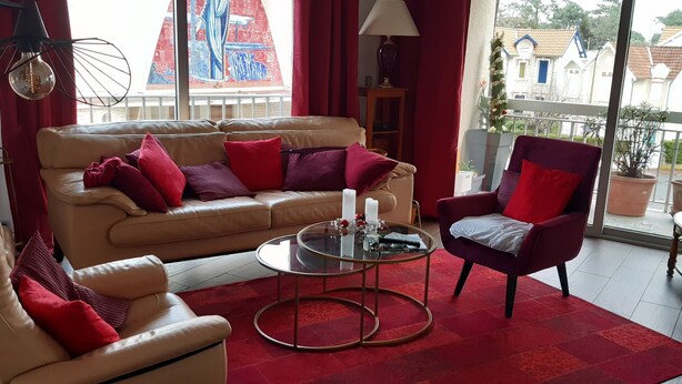A living room with a beige sofa, red cushions, a round glass coffee table, and a red rug.