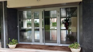 A modern building entrance with glass doors, potted plants, and a concrete pathway.