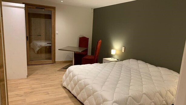 Un dormitorio con una cama grande, un escritorio, una silla y una puerta que da a otra habitación.