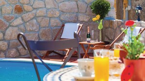 A poolside area with stone walls, lounge chairs, a table with drinks, and a small potted plant. - Lovely home in Grizane (Grizane)