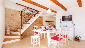 A dining area with a stone wall, wooden staircase, white furniture, and a TV mounted on the wall. - Lovely home in Grizane (Grizane)