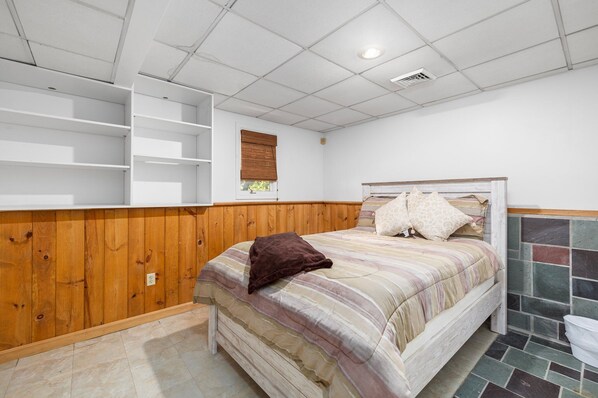 Un dormitorio con cama, paneles de madera, una ventana con persianas y suelo de baldosas.