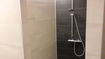 Une petite douche moderne avec un mur recouvert de carreaux foncés et un sol de couleur claire.