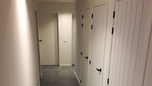 A hallway with grey tiled flooring and white walls. There are multiple doors with black handles on the right side. - La Cigale, beautiful villa with infinity pool and breathtaking views  (Chassagnes)