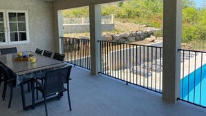 A covered patio with a dining table and chairs, a stone wall, and a view of a swimming pool and greenery. - La Cigale, beautiful villa with infinity pool and breathtaking views  (Chassagnes)