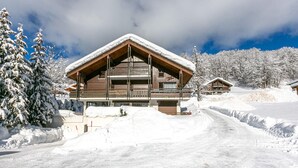 Una cabaña de madera con techo inclinado, rodeada de árboles cubiertos de nieve y un cielo despejado.