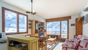 Interior acogedor de una cabaña con una mesa de madera, sillas, un sofá y una zona de cocina.