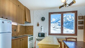 Cocina compacta con armarios de madera, refrigerador, microondas y estufa. Se ve una ventana con vistas a un paisaje montañoso nevado.