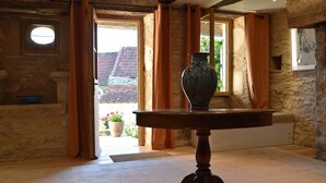 Quarto com parede de pedra, mesa de madeira com um vaso e vista para um jardim através de uma porta aberta.