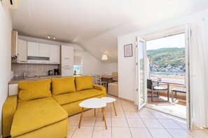 Un salón moderno con un sofá amarillo, una mesita blanca y un balcón con vistas a un paisaje montañoso.