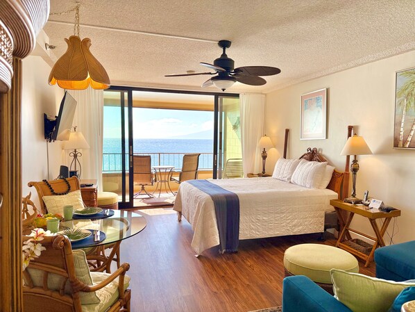 A hotel room with a bed, a balcony with a view, a dining table, and a TV.