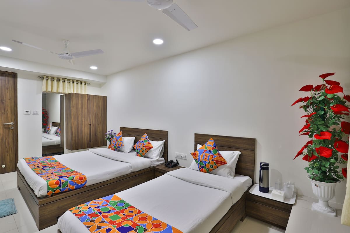 A hotel room with two beds, a ceiling fan, a nightstand, a vase with red flowers, and a mirror.