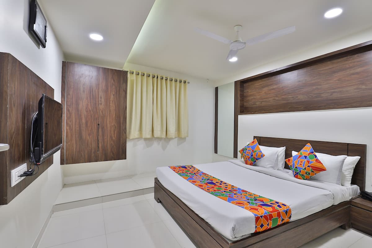 A bedroom with a bed, a ceiling fan, a TV mounted on the wall, and a window with curtains.