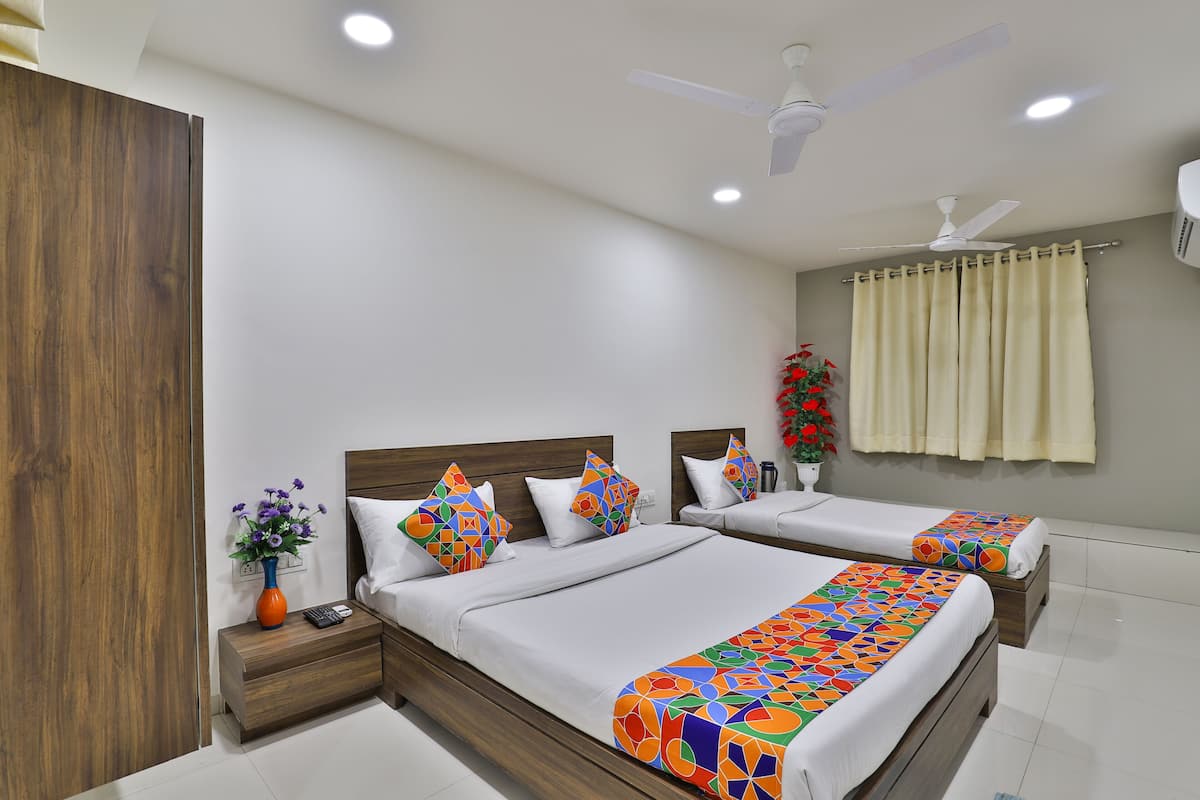 A hotel room with two beds, a nightstand, a vase with flowers, a ceiling fan, and a window with curtains.