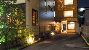 A building with a covered walkway, a door with Japanese characters, and a small garden area with plants. - Kagetsu Ryokan (Shizuoka)