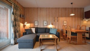 A cozy living room with a sectional sofa, a wooden coffee table, and a dining area with wooden chairs and a table.