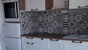 Ett modernt kök med vita skåp, en mönstrad väggbeklädnad bakom arbetsbänken och ett träbord med en stol.