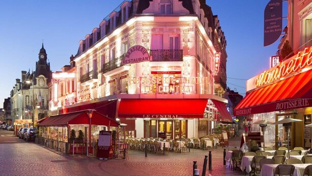 Ett hotell med en centralt belägen restaurang, uteservering och ett klocktorn i bakgrunden.