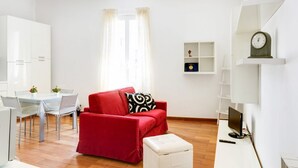 A modern living room with a red sofa, a glass dining table, and a white TV stand.