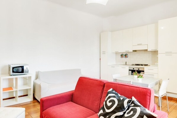 A compact living space with a red sofa, a white dining table, and a kitchenette.