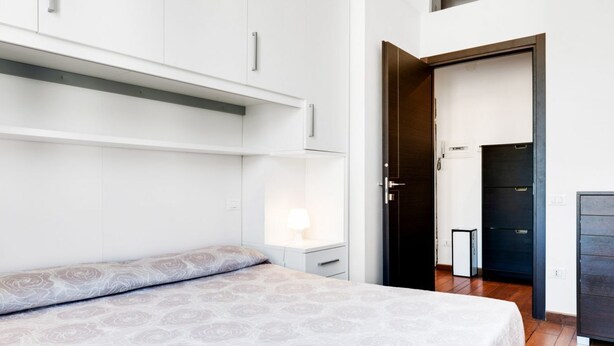 A bedroom with a bed, a nightstand, a wardrobe, and a door leading to another room.