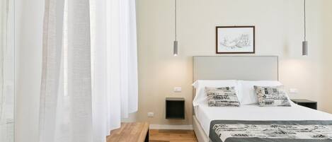 Quarto com cama, mesas de cabeceira, um banco, um quadro na parede e uma luminária de teto.